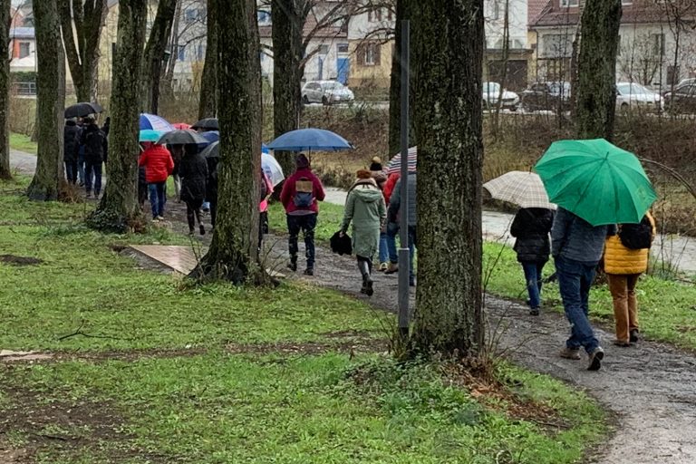 Personen laufen an der Eyach entlang mit Regenschirmen