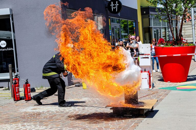 Eine riesige Flamme schießt aus einem Behälter, dahinter ist halb verdeckt ein Mann in Feuerwehrkleidung zu sehen