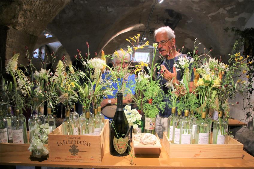 Zu sehen ist ein Arrangement aus Blumen in Flaschen, dahinter stehen zwei Ausstellungsbesucher