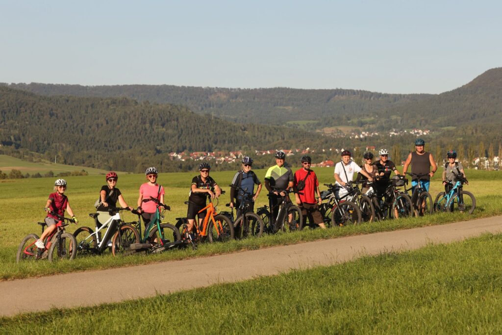 Eine Gruppe Radlerinnen und Radler steht mit ihren E-Bikes in einer Wiese, im Hintergrund die Balinger Berge